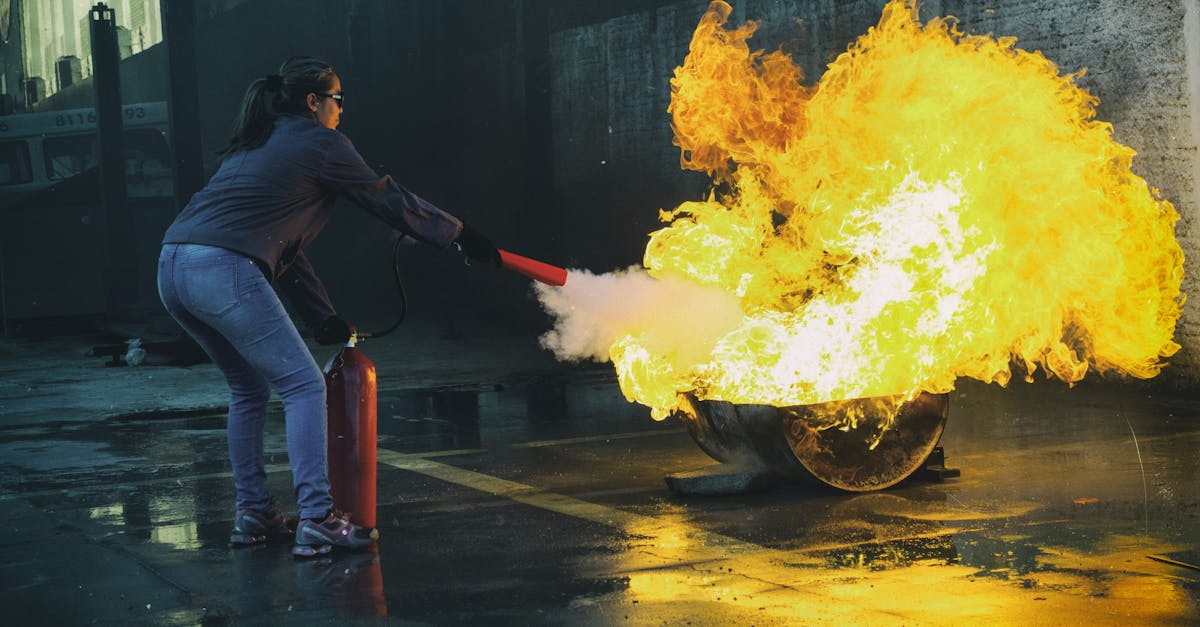 A woman uses a fire extinguisher to put out a large flame in an outdoor setting, showcasing fire safety.